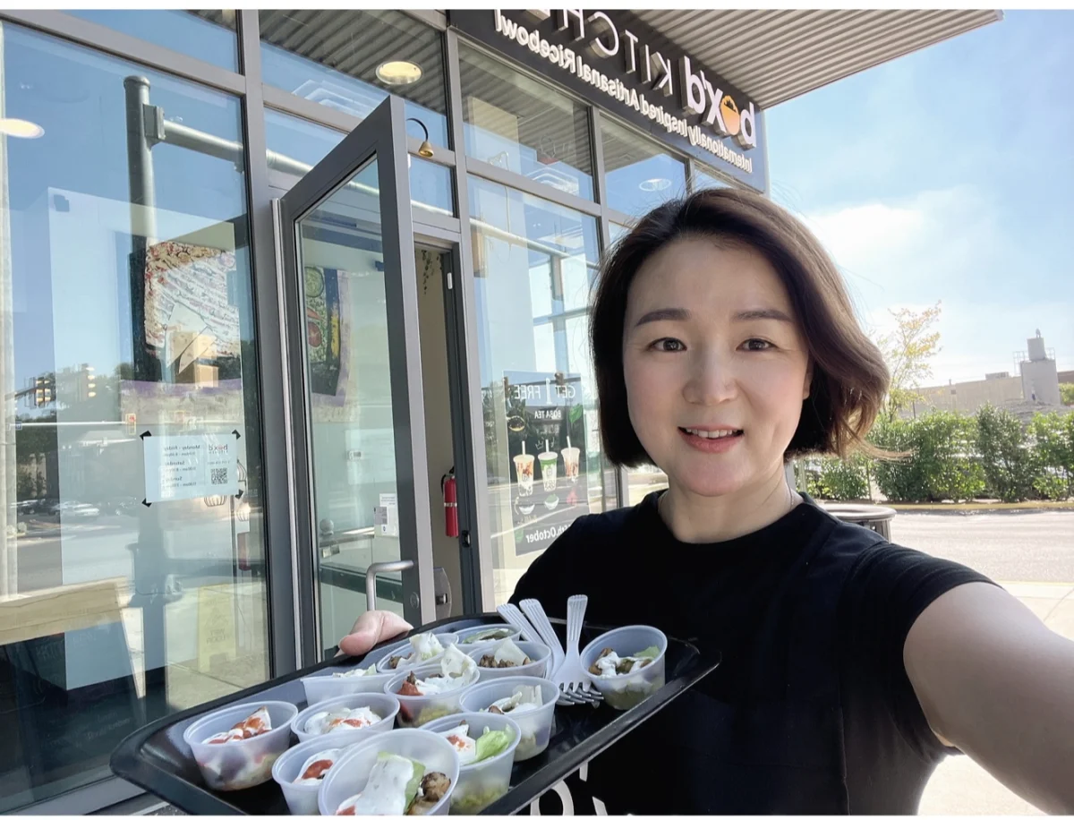 Nayoung Yum welcoming guests with a tray of food samples outside Box’d Kitchen